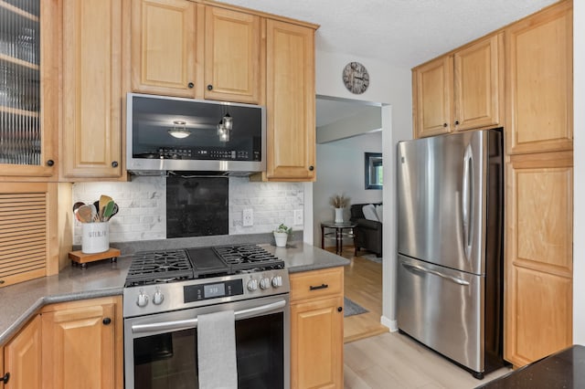 kitchen with stainless steel appliances, backsplash, light brown cabinetry, and a textured ceiling