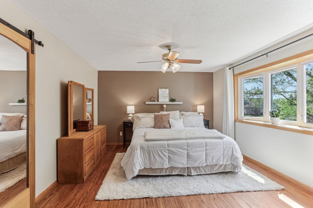 bedroom with a barn door, wood finished floors, baseboards, a textured ceiling, and ceiling fan