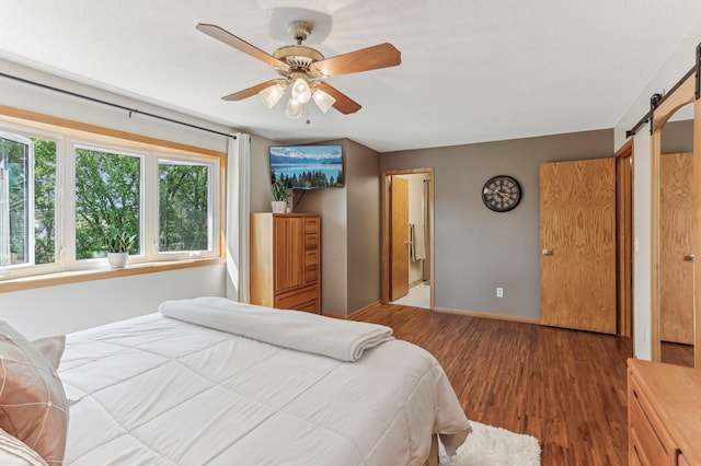 bedroom featuring a barn door, wood finished floors, baseboards, and ceiling fan