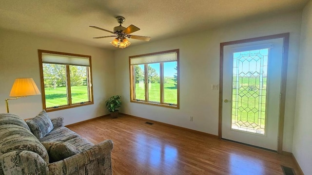 living area featuring wood finished floors, ceiling fan, baseboards, and a textured ceiling