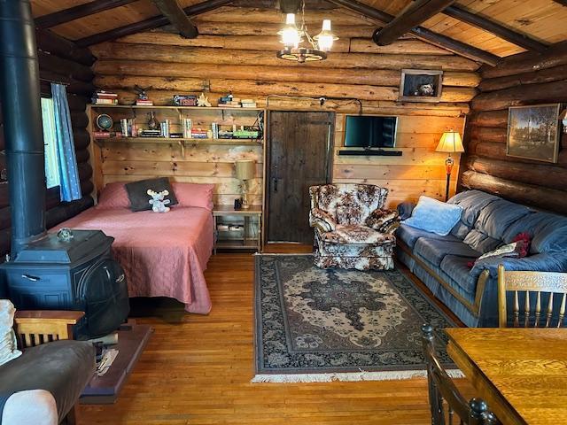 bedroom featuring a wood stove, wood ceiling, log walls, and lofted ceiling with beams