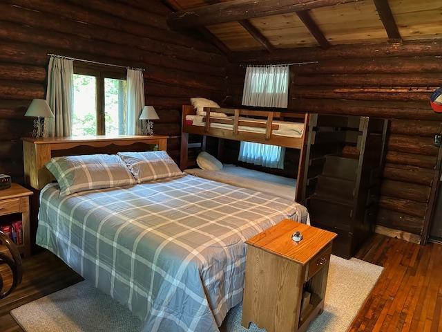 bedroom with vaulted ceiling with beams, log walls, wooden ceiling, and hardwood / wood-style flooring