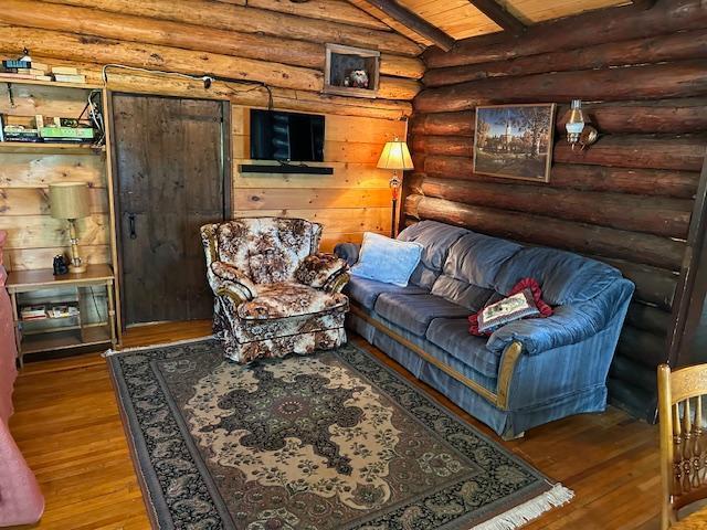 living area with log walls, hardwood / wood-style flooring, wood ceiling, and vaulted ceiling with beams