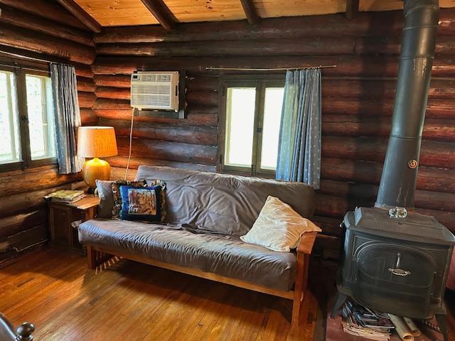 living area with a wall mounted AC, rustic walls, hardwood / wood-style flooring, beamed ceiling, and a wood stove