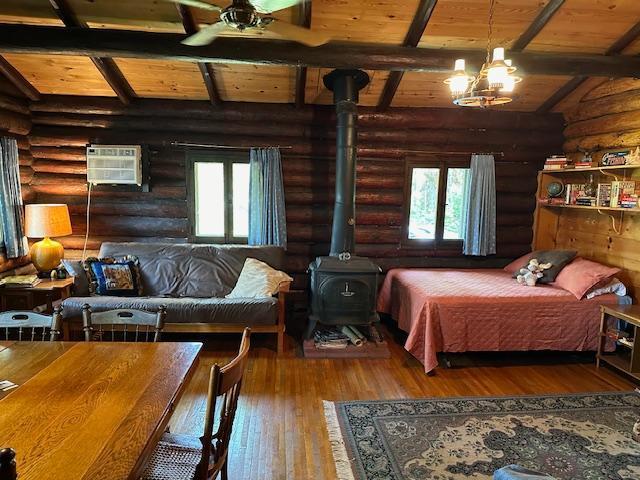 bedroom with beamed ceiling, a wood stove, and log walls