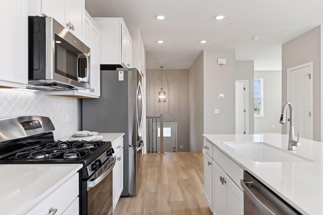 kitchen featuring appliances with stainless steel finishes, a sink, light wood-style floors, light countertops, and recessed lighting