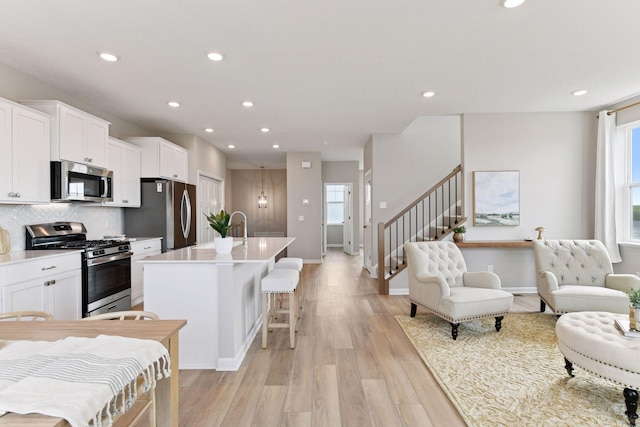 kitchen with stainless steel appliances, plenty of natural light, a center island with sink, white cabinets, and recessed lighting