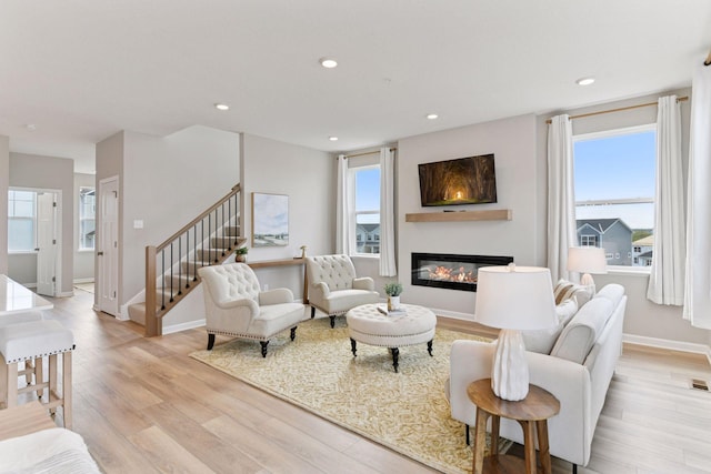 living room with light wood-style flooring, a glass covered fireplace, recessed lighting, baseboards, and stairway