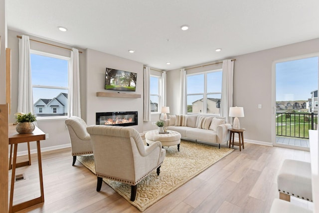 living area with light wood-type flooring, a glass covered fireplace, baseboards, and recessed lighting