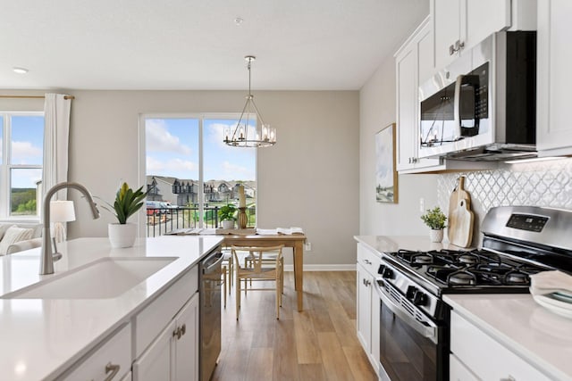 kitchen with appliances with stainless steel finishes, a sink, light wood-type flooring, a chandelier, and light countertops