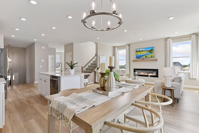dining room featuring recessed lighting, light wood-type flooring, a glass covered fireplace, baseboards, and a chandelier
