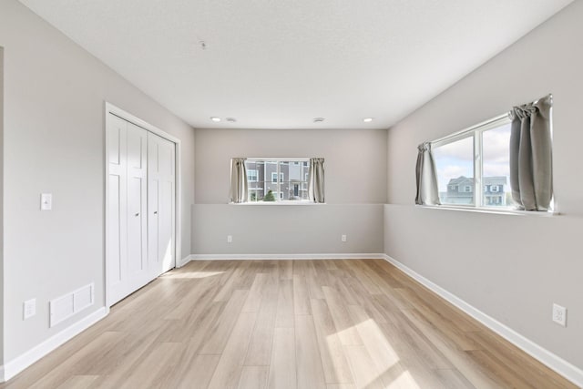 unfurnished bedroom featuring multiple windows, light wood-type flooring, baseboards, and recessed lighting