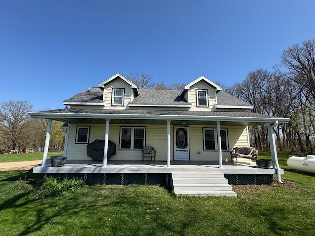 farmhouse-style home with a porch, roof with shingles, and a front lawn