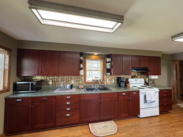 kitchen with white electric stove, a sink, stainless steel microwave, under cabinet range hood, and open shelves