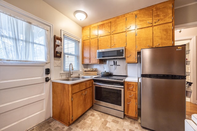kitchen with stainless steel appliances, a sink, brown cabinetry, and light countertops