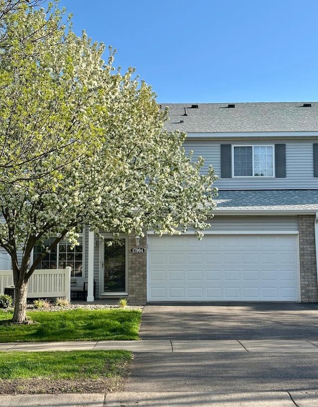 view of front of house featuring an attached garage, a shingled roof, brick siding, and driveway