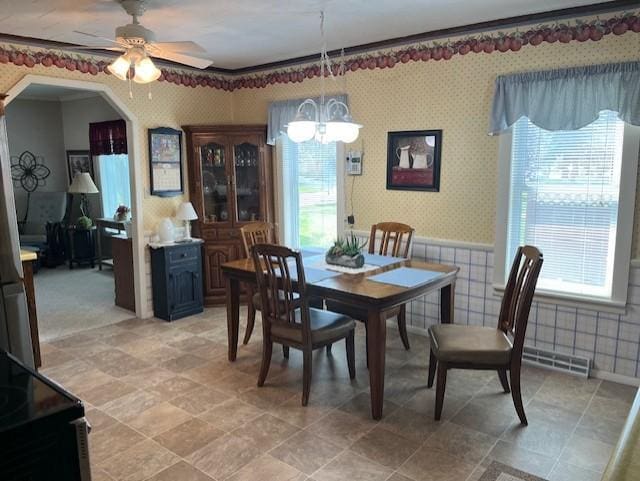 dining area featuring arched walkways, wallpapered walls, a wainscoted wall, and ceiling fan with notable chandelier