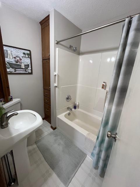 bathroom with a textured ceiling and shower / bathtub combination with curtain