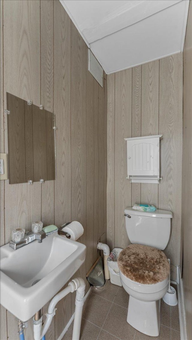 bathroom with toilet, wood walls, and a sink
