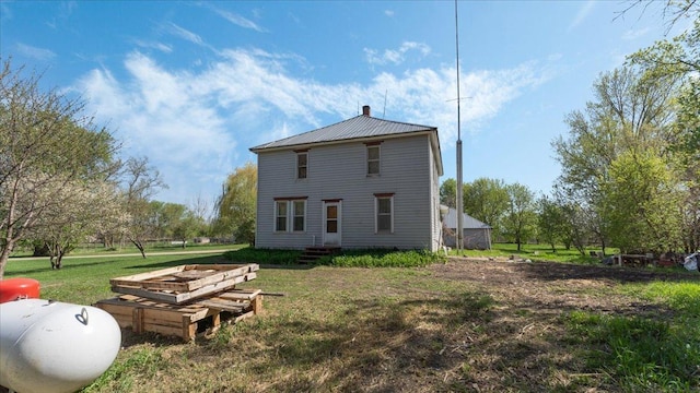rear view of house with a chimney, a lawn, metal roof, and entry steps
