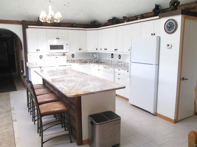 kitchen with a center island, white cabinetry, light stone countertops, arched walkways, and white appliances