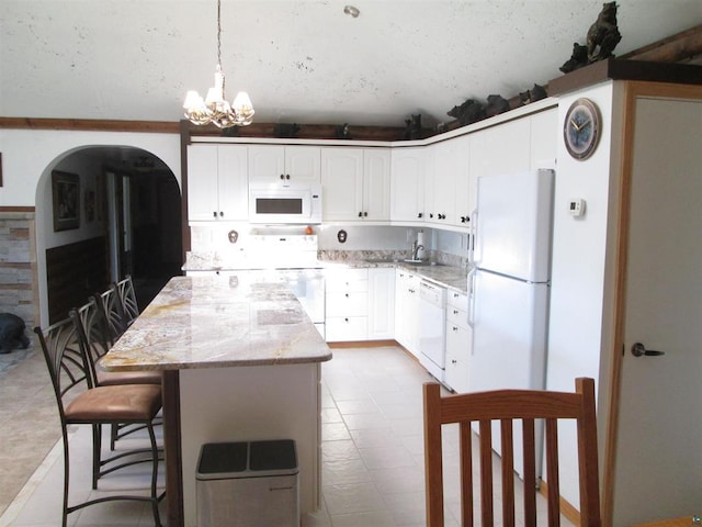kitchen with white appliances, an inviting chandelier, arched walkways, a center island, and light stone countertops