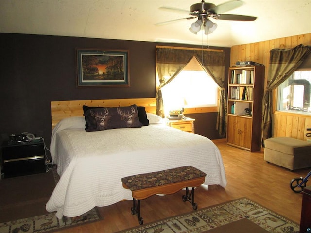 bedroom featuring multiple windows, light wood-style floors, wooden walls, and ceiling fan