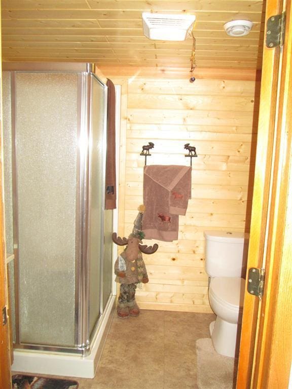 bathroom featuring toilet, a stall shower, tile patterned floors, wood walls, and wooden ceiling
