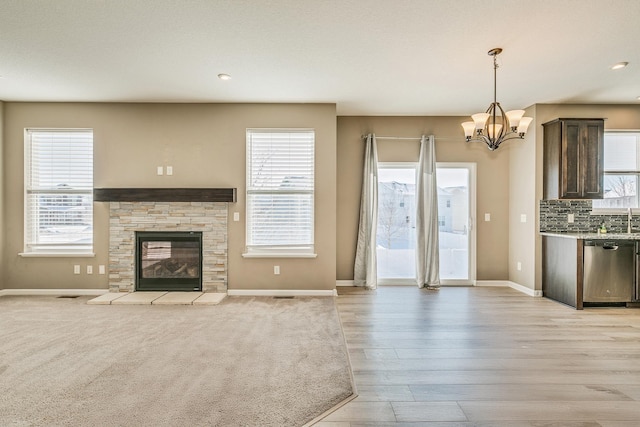unfurnished living room featuring a notable chandelier, light wood-type flooring, baseboards, a stone fireplace, and recessed lighting