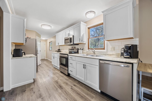 kitchen with stainless steel appliances, a sink, light wood finished floors, tasteful backsplash, and plenty of natural light