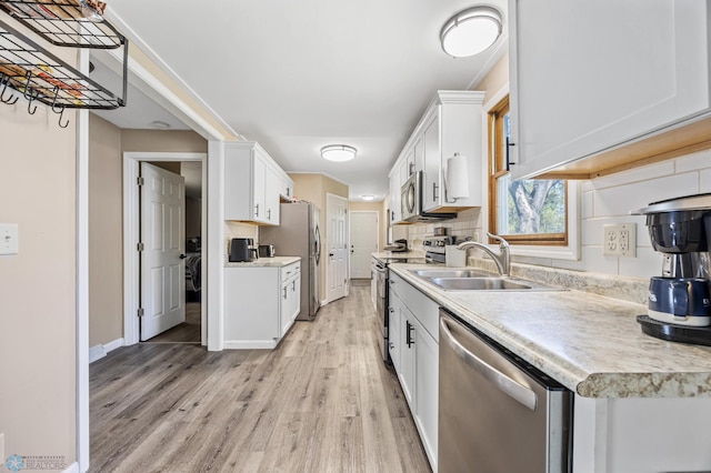 kitchen with appliances with stainless steel finishes, light wood finished floors, light countertops, a sink, and white cabinetry