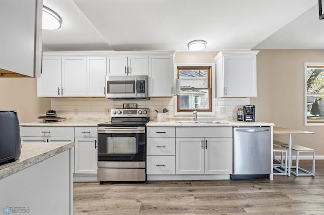 kitchen featuring stainless steel appliances, a sink, light wood finished floors, and white cabinets