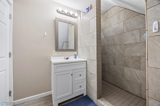 full bathroom with vanity, a tile shower, baseboards, and wood finished floors