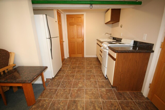 kitchen featuring a sink, white appliances, dark countertops, and dark tile patterned floors