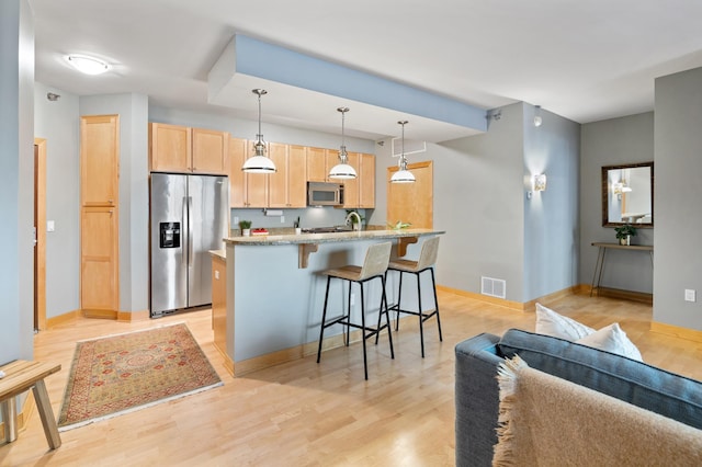 kitchen featuring appliances with stainless steel finishes, light brown cabinetry, a breakfast bar area, light stone counters, and light wood-type flooring
