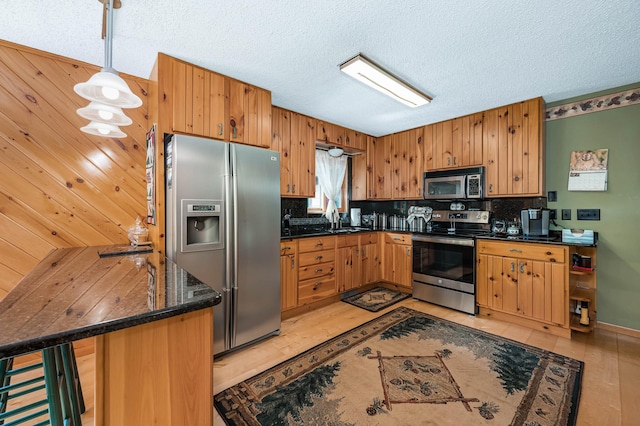 kitchen featuring a textured ceiling, hanging light fixtures, a sink, decorative backsplash, and appliances with stainless steel finishes