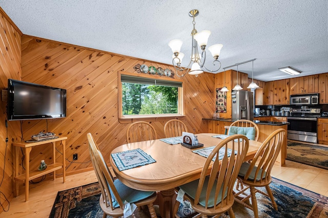dining room featuring an inviting chandelier, a textured ceiling, wooden walls, and light wood-style floors