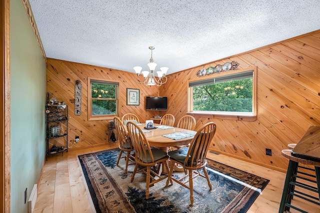 dining area featuring wood walls, a chandelier, a textured ceiling, and hardwood / wood-style flooring