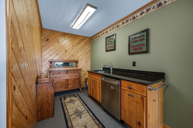 kitchen with a sink, brown cabinetry, wood walls, a textured ceiling, and dishwasher