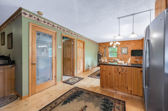 kitchen featuring freestanding refrigerator, wooden walls, an inviting chandelier, and light wood-style floors