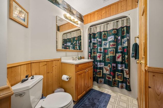 full bath featuring a textured ceiling, toilet, wainscoting, wooden walls, and vanity