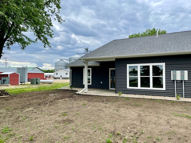rear view of property featuring central AC unit, a patio, and a shingled roof