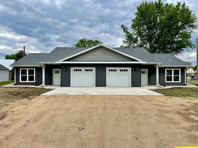 single story home featuring a garage, dirt driveway, and a shingled roof