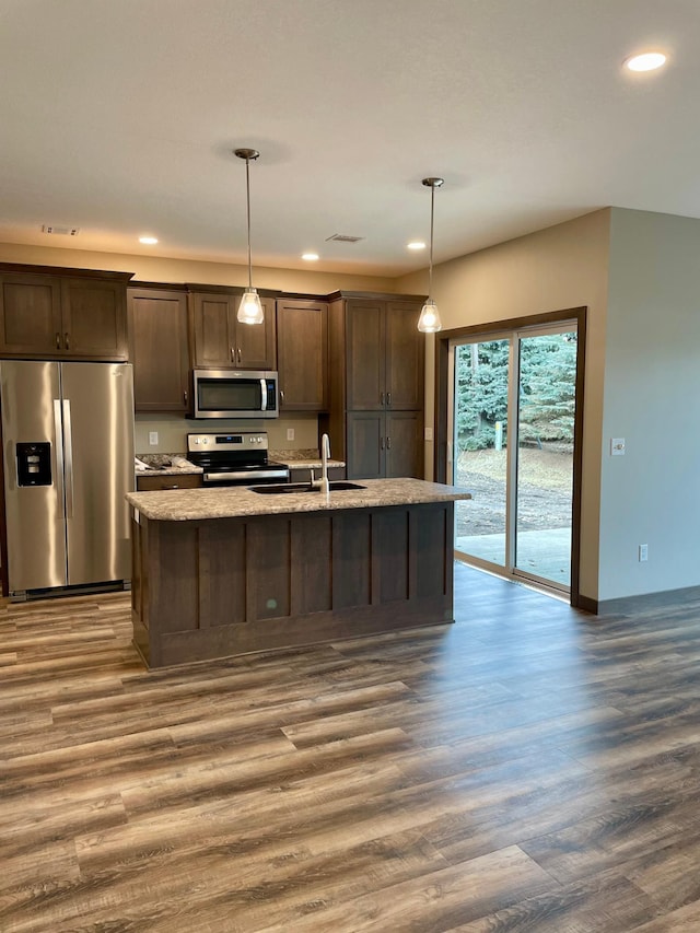 kitchen with a sink, dark brown cabinetry, a center island with sink, appliances with stainless steel finishes, and dark wood-style floors