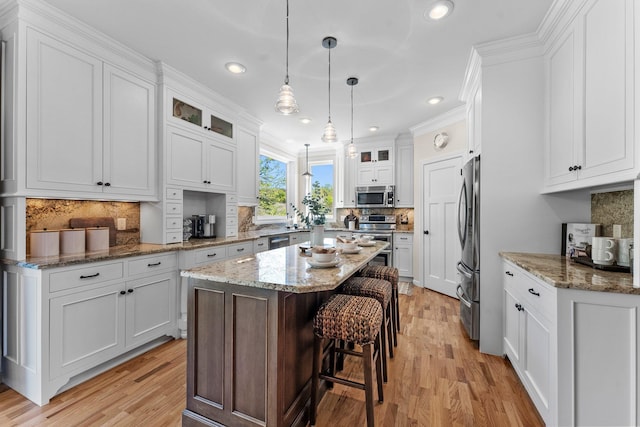 kitchen featuring appliances with stainless steel finishes, tasteful backsplash, a kitchen island, white cabinetry, and light wood finished floors