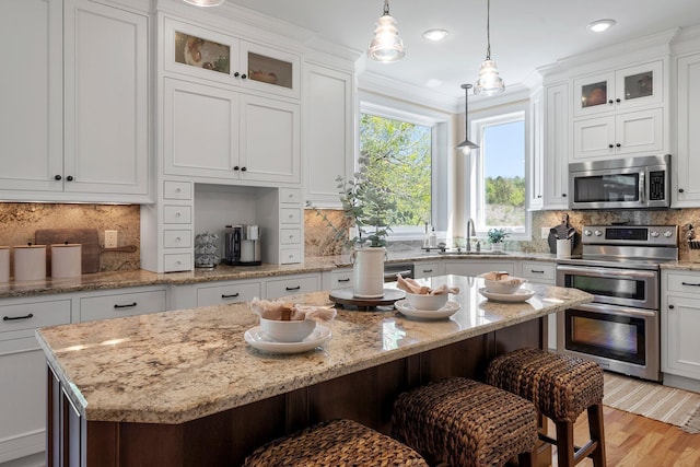 kitchen featuring stainless steel appliances, a sink, a breakfast bar, white cabinetry, and pendant lighting