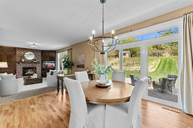 dining space featuring a chandelier, wood finished floors, and a brick fireplace
