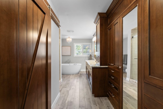 full bath featuring vanity, a soaking tub, wood finished floors, and baseboards