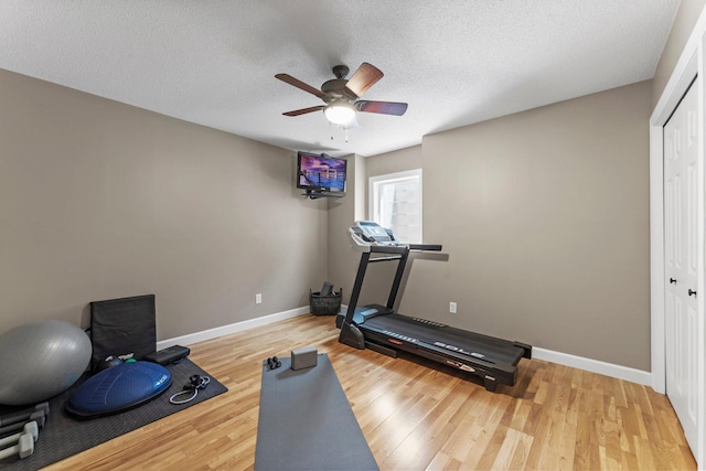 workout area with a ceiling fan, wood finished floors, baseboards, and a textured ceiling