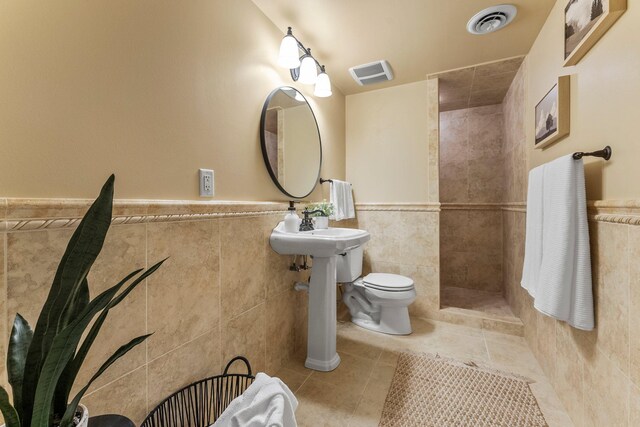 bathroom with tile walls, a tile shower, tile patterned floors, a wainscoted wall, and toilet